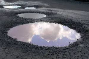 Puddles on a muddy road reflect a blue sky with fluffy clouds