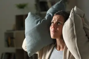 A woman indoors holds pillows to her ears