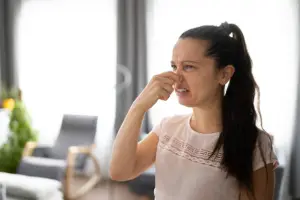 A woman with a ponytail pinches her nose while grimacing