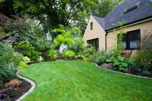 A charming backyard with a tidy lawn is bordered by lush green shrubs and trees next to a cozy